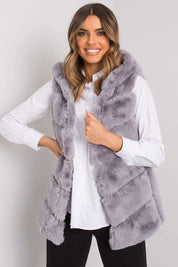 Woman wearing gray faux fur vest over white shirt, smiling.