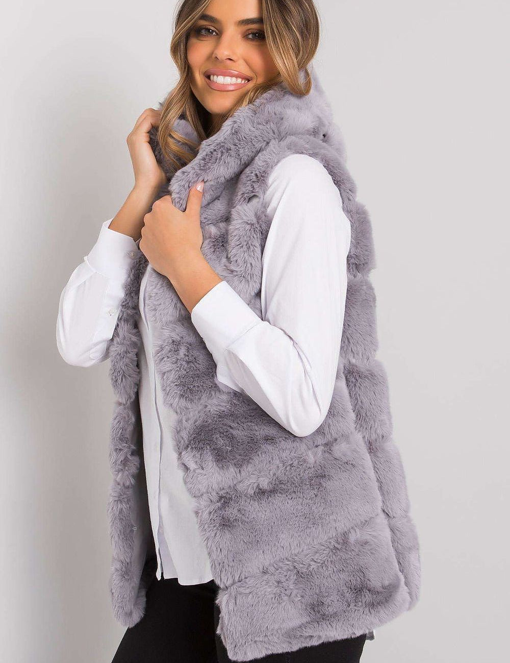Woman wearing a gray faux fur sleeveless vest over a white blouse, showcasing a stylish and cozy winter fashion look.