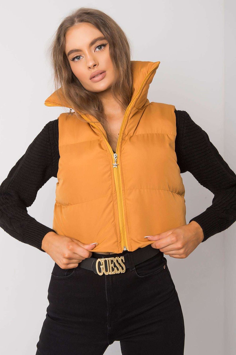 Woman wearing an orange zip vest with high collar and black sleeves, featuring a Guess belt buckle.