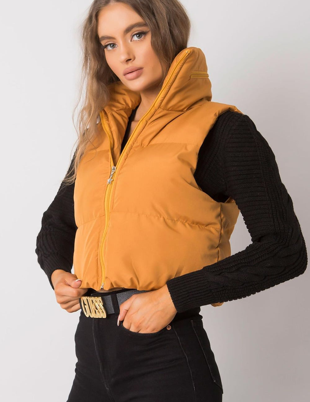 Woman wearing an orange puffer vest over a black sweater, showcasing a casual fall fashion look.