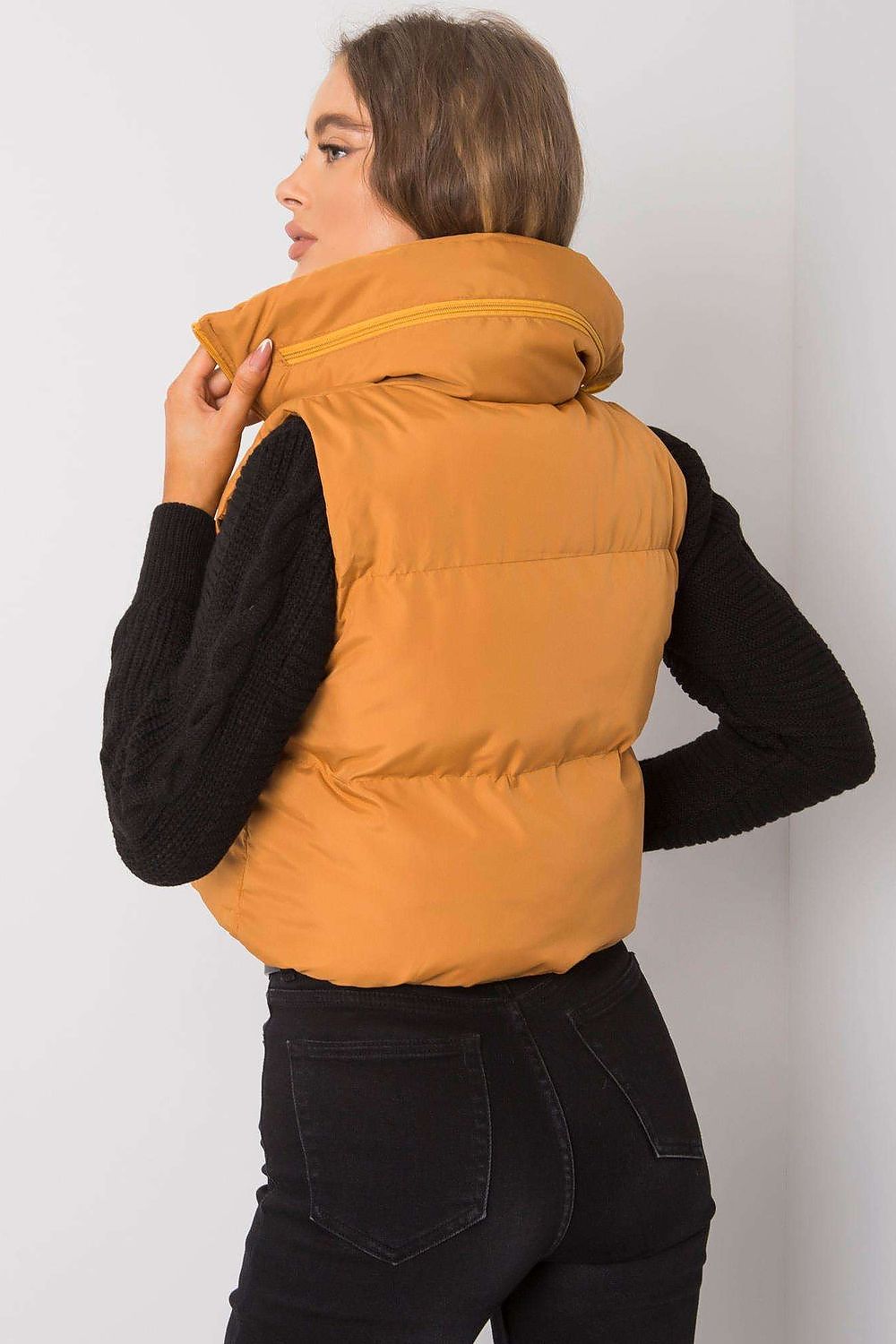 Back view of a woman wearing a khaki zip vest with a concealed hood, paired with black sleeves, showcasing a casual style.