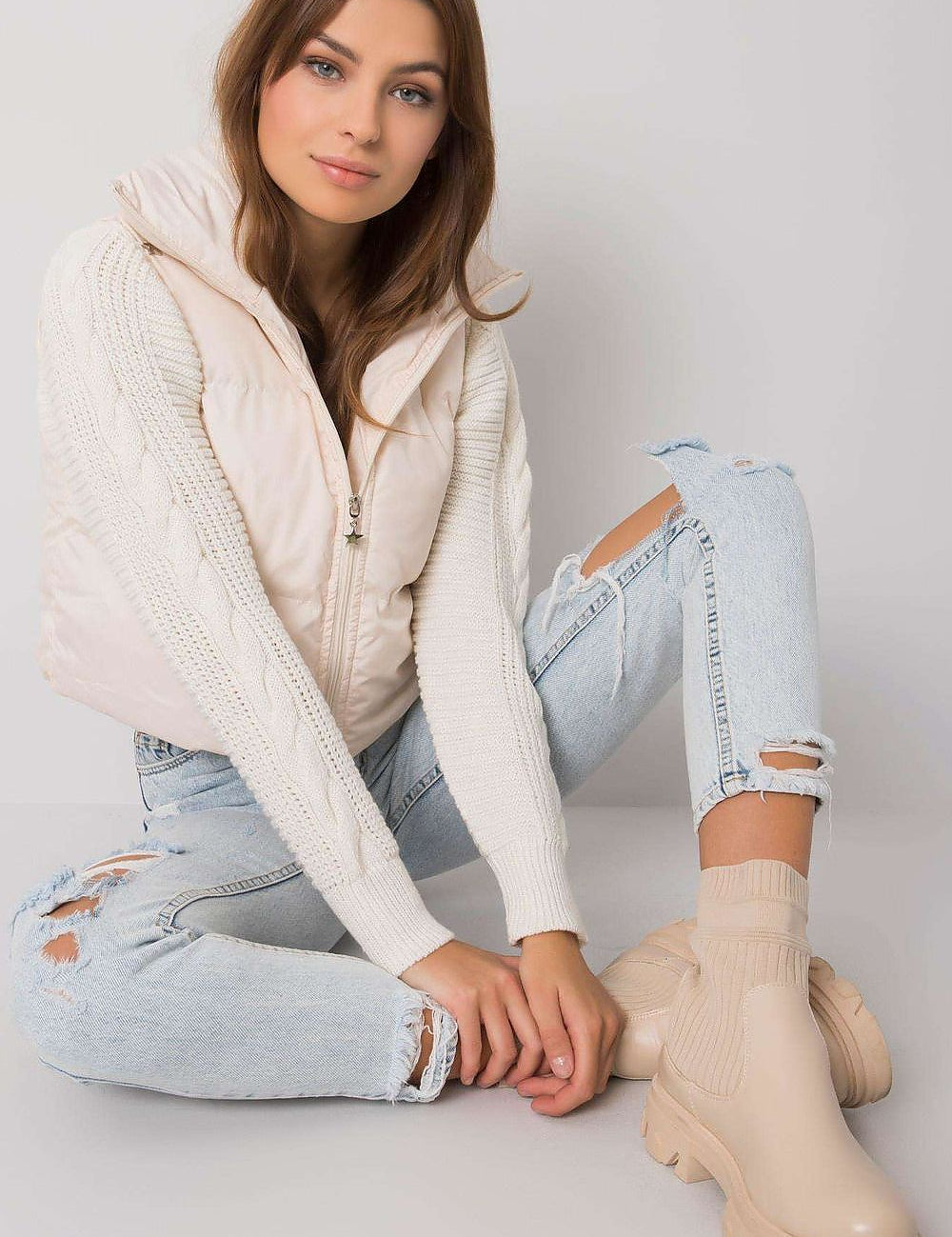 Woman wearing a white knit sweater with ripped jeans and beige boots