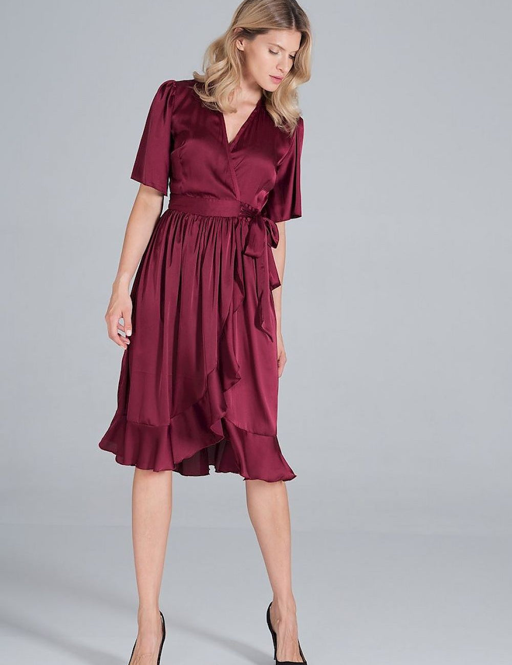 Woman wearing a burgundy satin midi wrap dress with a tie waist and flounce hemline.