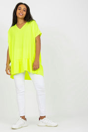 Model wearing a lime green plus size tunic with frilled hem and heart-shaped neckline, paired with white leggings and sneakers.