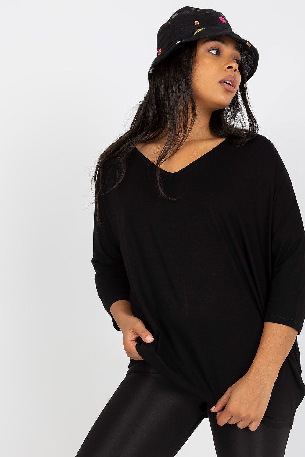 Woman wearing a black 3/4 sleeve blouse with a sweetheart neckline, paired with leggings and a colorful bucket hat.