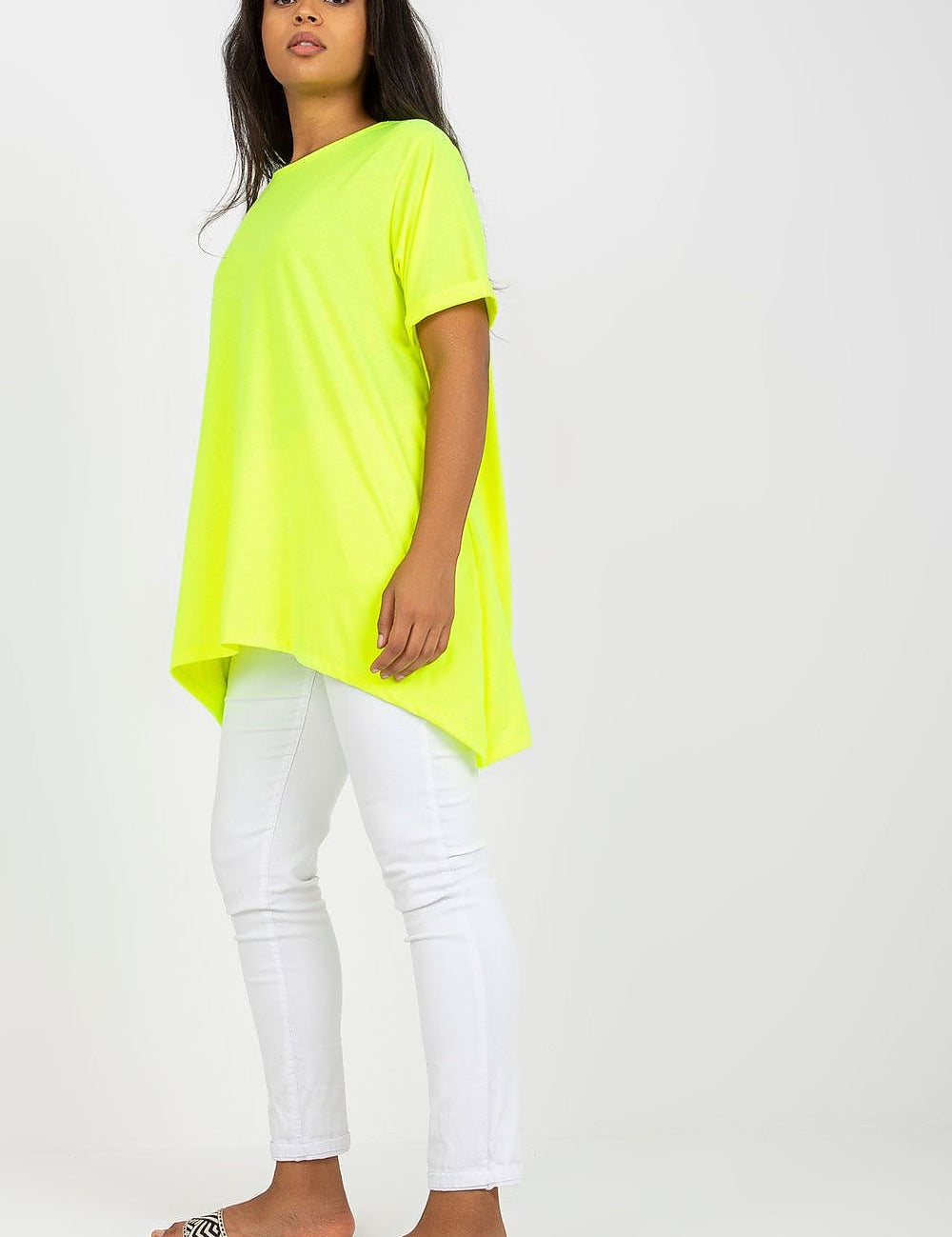 Woman wearing a neon yellow asymmetrical tunic with a relaxed fit and boat neckline, paired with white pants and slide sandals.
