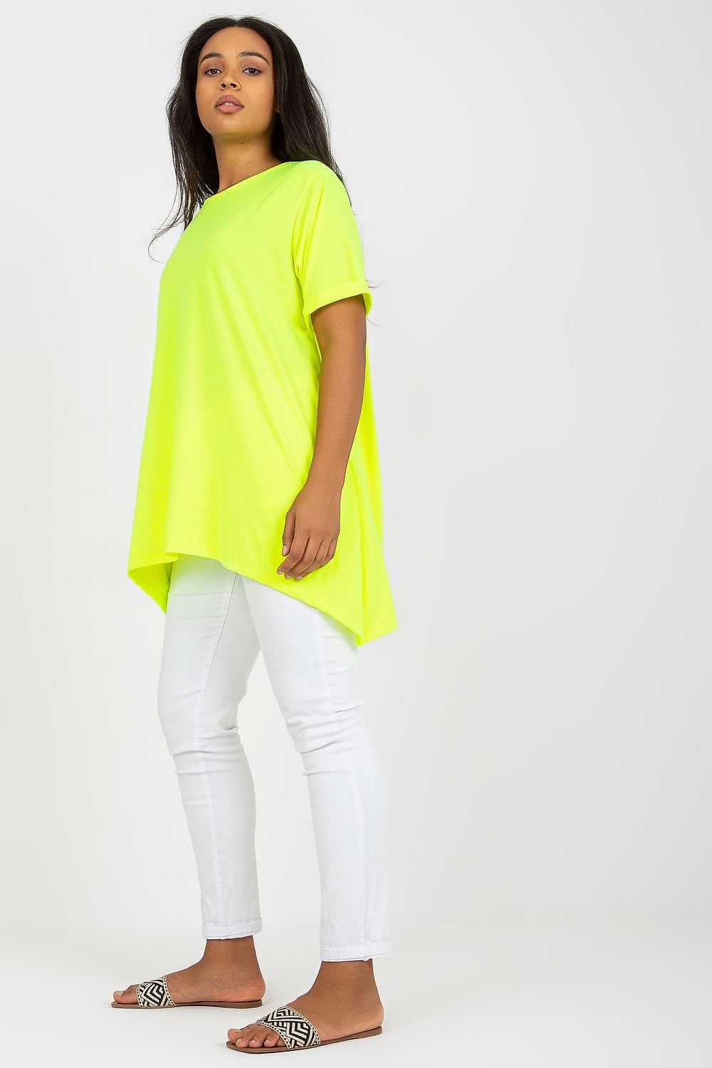 Woman wearing a neon yellow asymmetrical tunic with a relaxed fit and boat neckline, paired with white pants and slide sandals.
