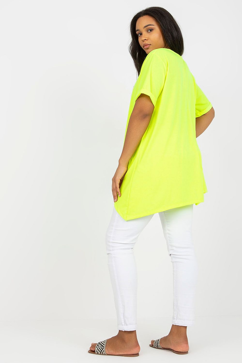 Plus size model wearing bright yellow Velenaria tunic with asymmetrical hem and white pants, showcasing relaxed fit and stylish design.