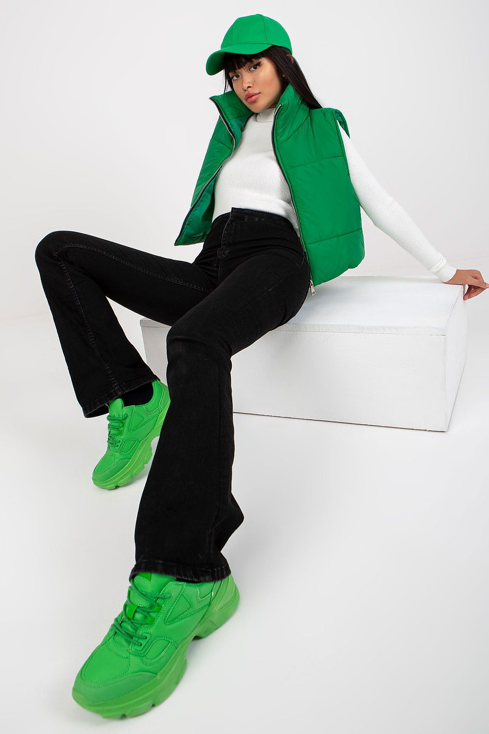 Woman wearing green Irdena Insulated Quilted Gilet Vest with black pants, white top, and matching green cap and sneakers, posing casually.