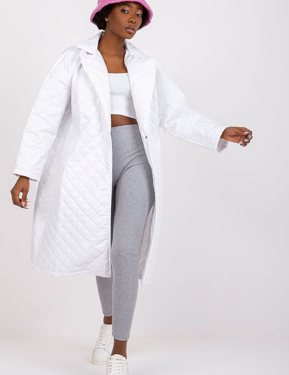Woman wearing Orlianne quilted transitional coat, white with side slip pockets, paired with grey leggings and pink bucket hat.