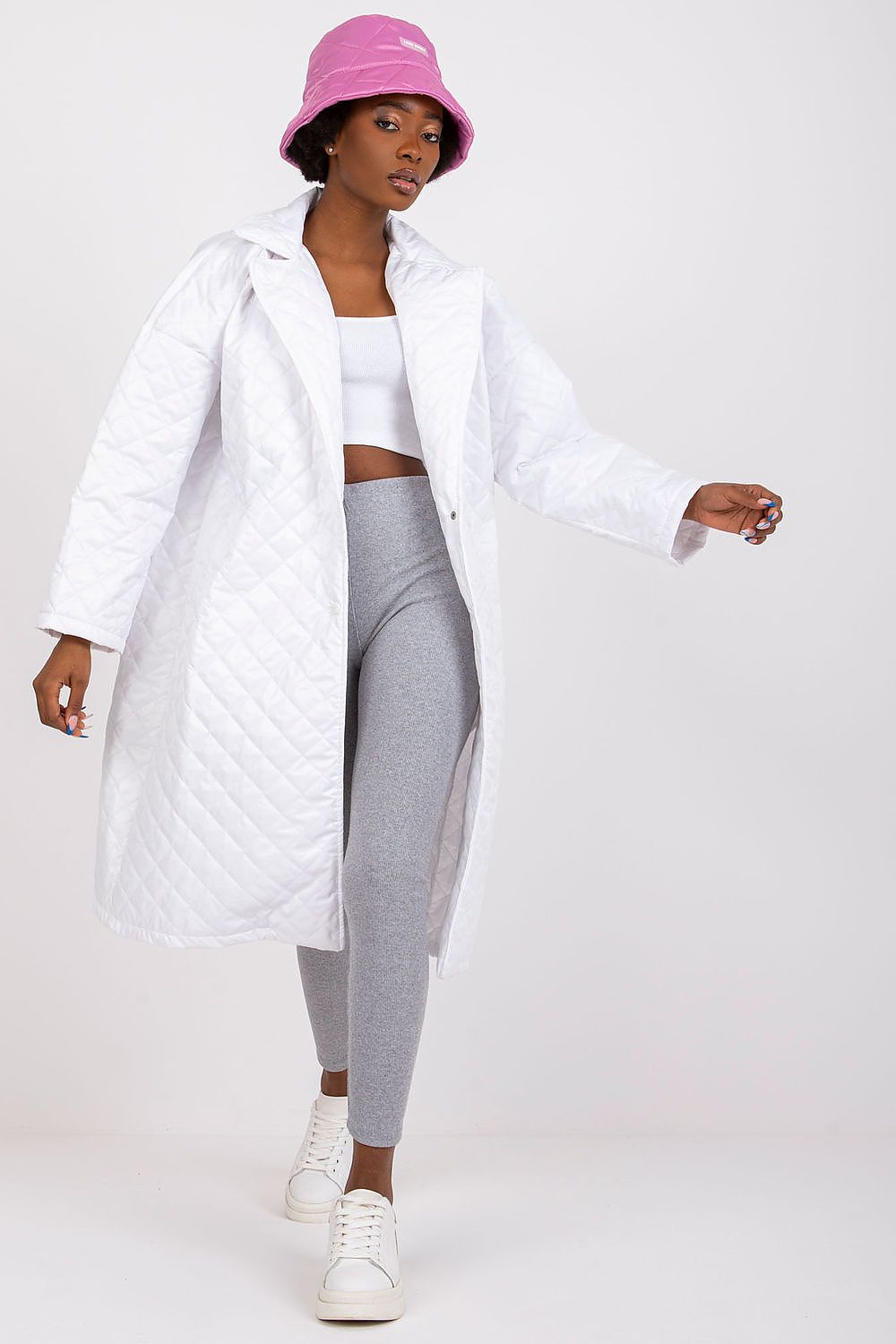 Woman wearing Orlianne quilted transitional coat, white with side slip pockets, paired with grey leggings and pink bucket hat.