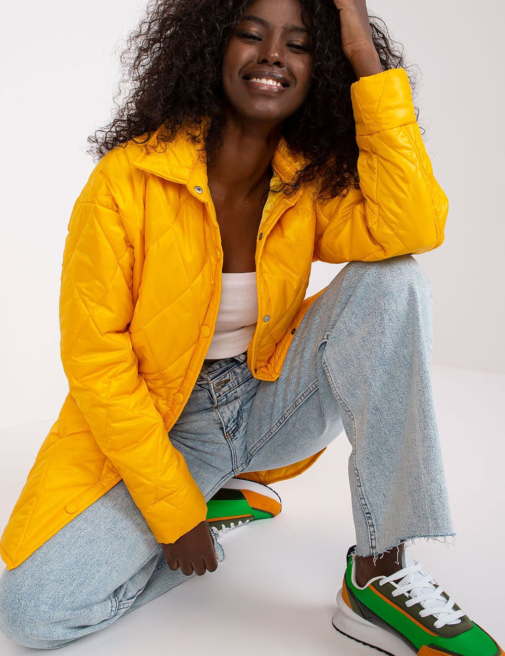 Woman modeling Cerenya quilted jacket with extended back, wearing casual jeans and sneakers, showcasing quilt design and vibrant color.
