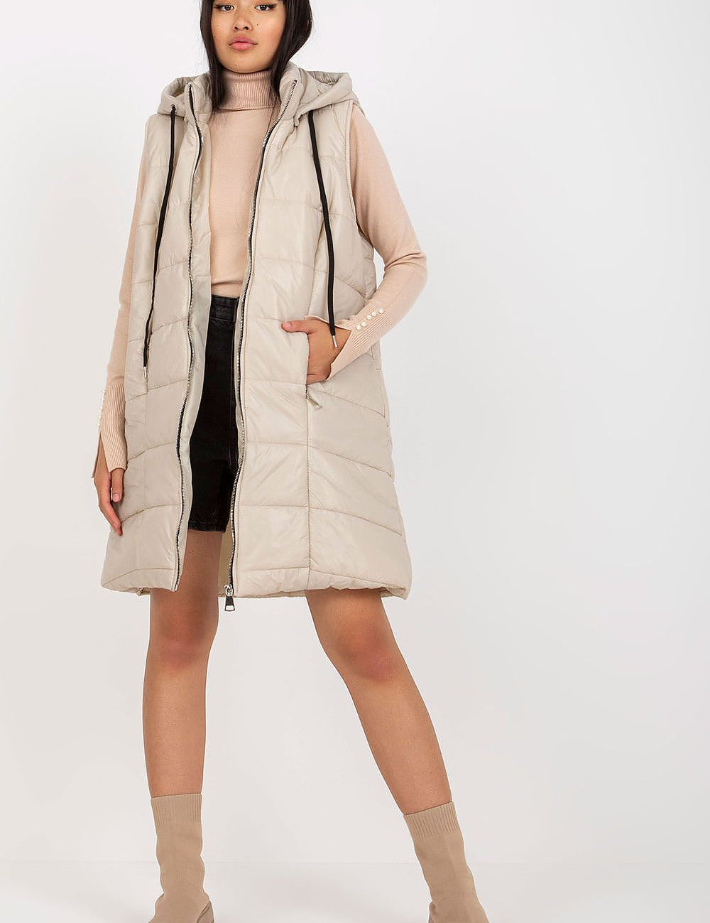 Woman wearing Evrendelle Quilted Longline Vest with detachable hood, showcasing its sleek silhouette and practical front pockets.