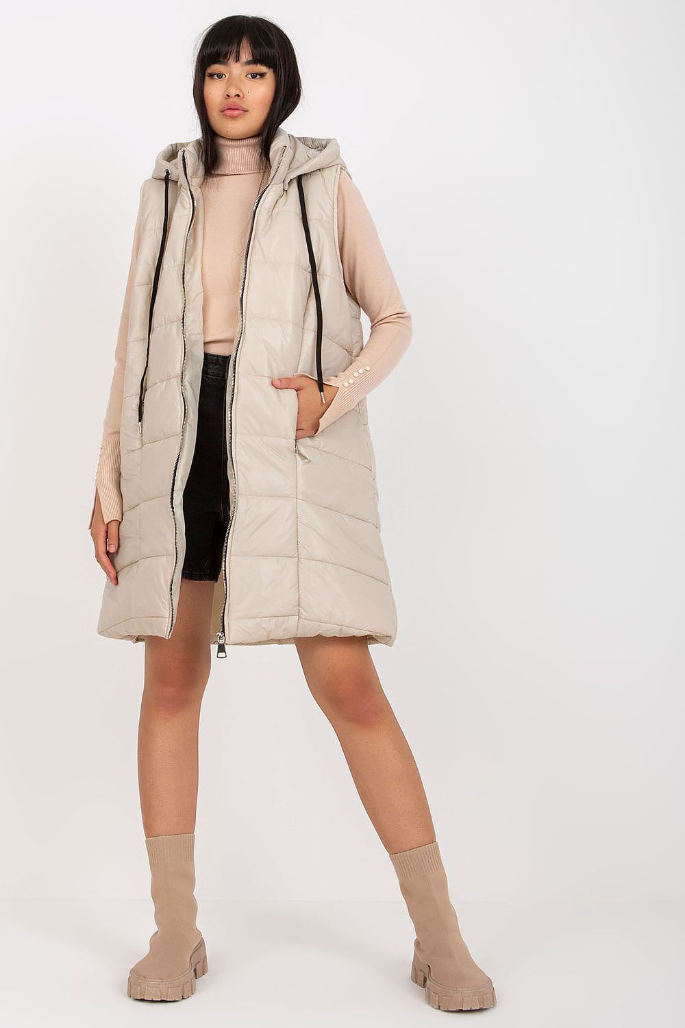 Woman wearing Evrendelle Quilted Longline Vest with detachable hood, showcasing its sleek silhouette and practical front pockets.