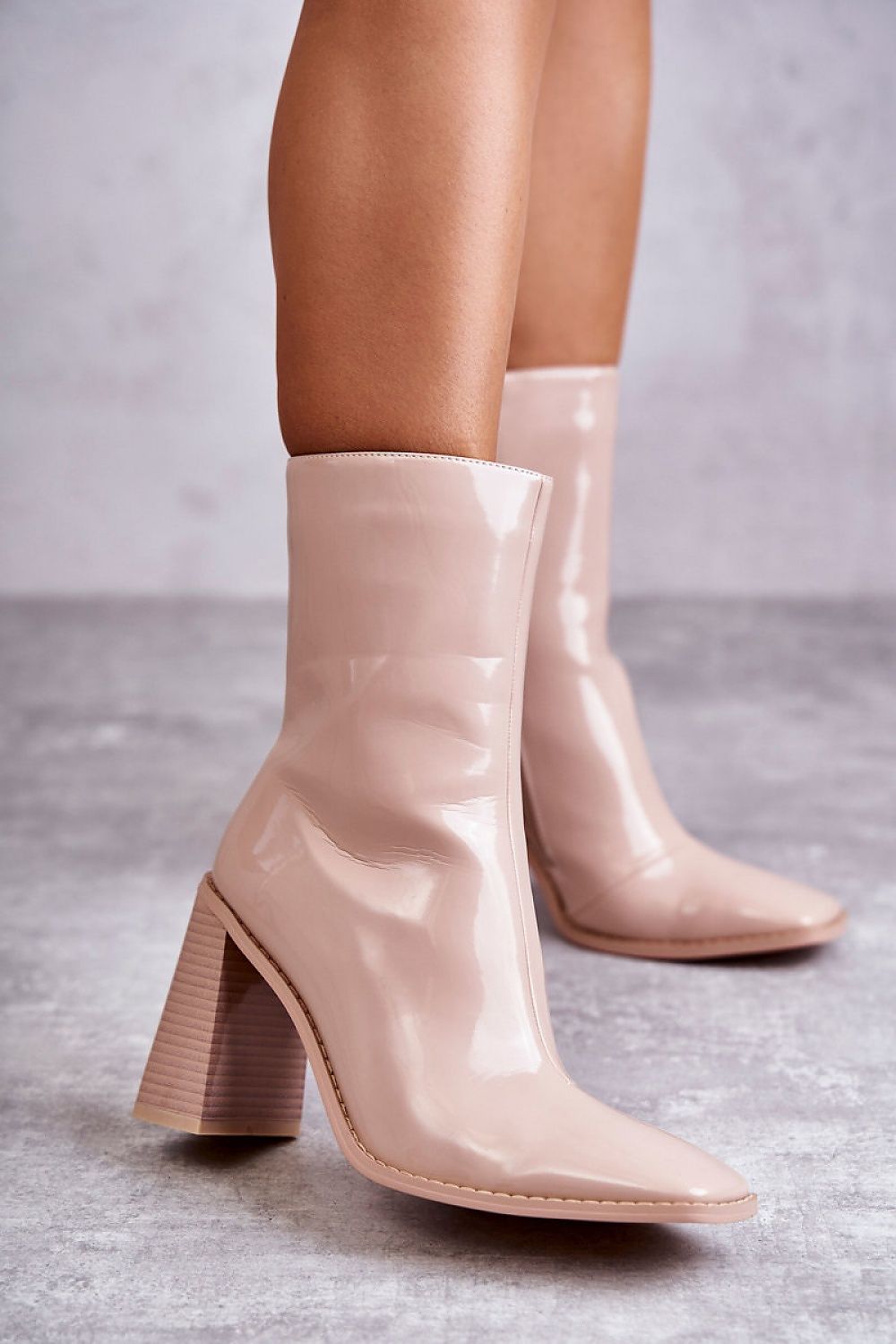 Woman wearing Lumirelle Glossflare Calf Silhouette boots with lacquer-finish and high stiletto heels on a textured floor.