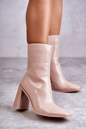 Woman wearing Lumirelle Glossflare Calf Silhouette boots with lacquer-finish and high stiletto heels on a textured floor.