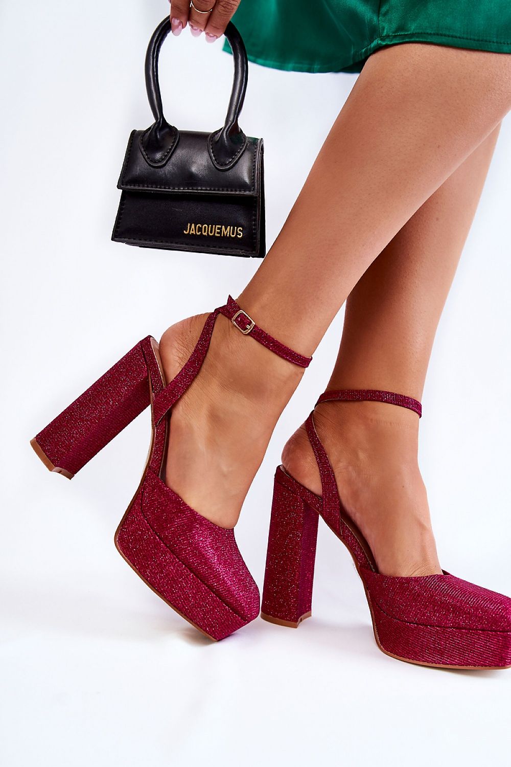 Woman wearing glittery red platform sandals with ankle strap, carrying a small black handbag, showcasing elegant evening footwear.