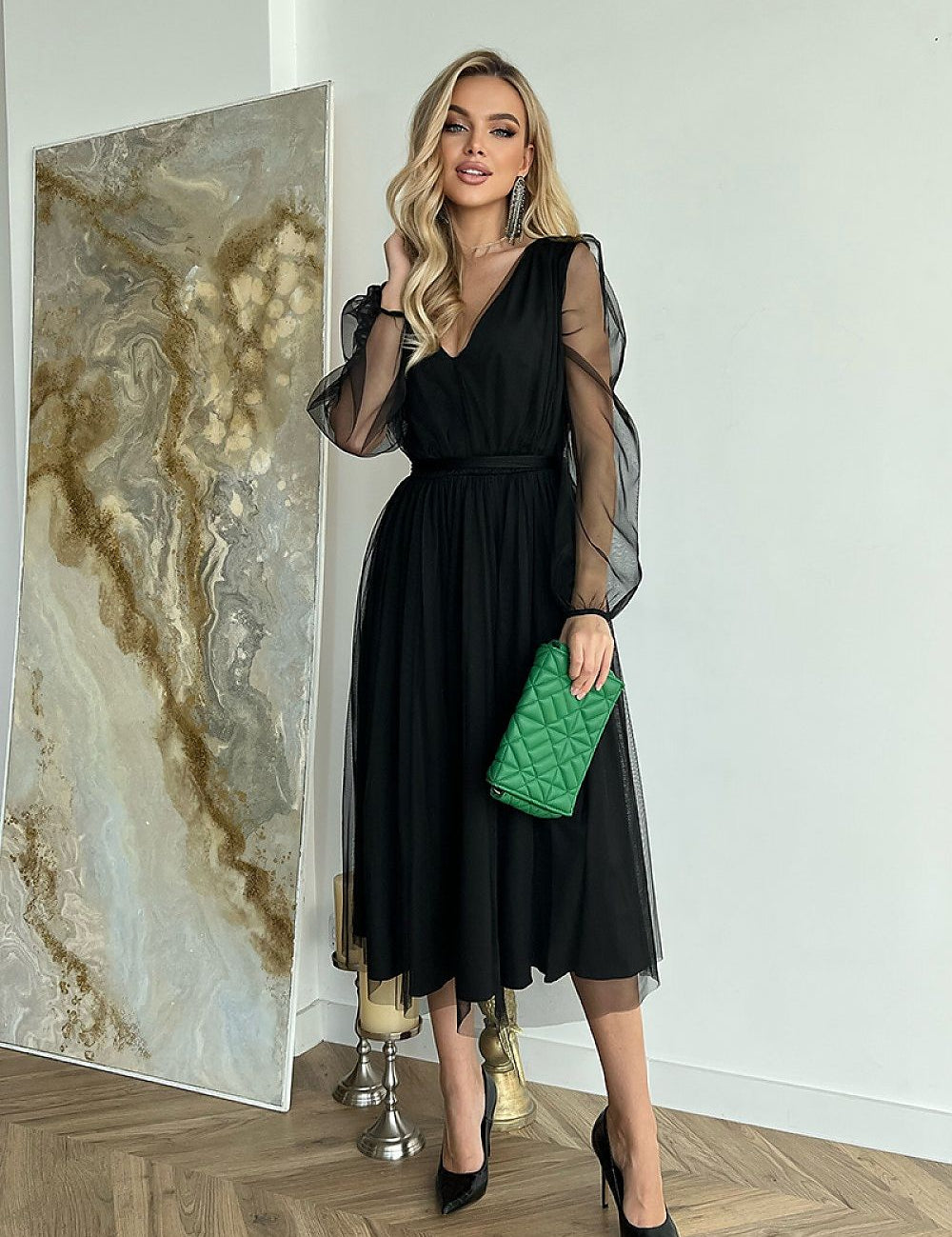 Woman wearing Marleia Mesh-Layered Evening Midi Dress with sheer sleeves, holding a green clutch in a stylish indoor setting.