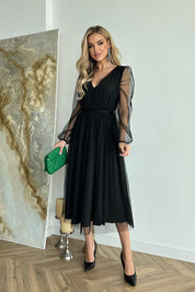 Woman wearing Marleia Mesh-Layered Evening Midi Dress with sheer sleeves and carrying a green bag.