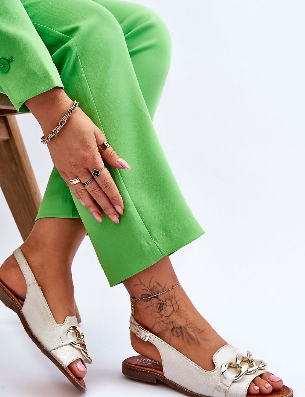 Woman wearing Dorellia Leather Flat Sandals with chain detail, paired with green pants.