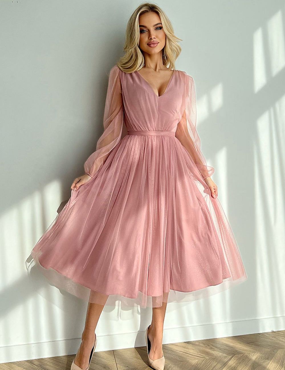 Woman wearing Marleia Mesh-Layered Evening Midi Dress in pink with sheer sleeves and flared skirt, standing against a sunlit wall.