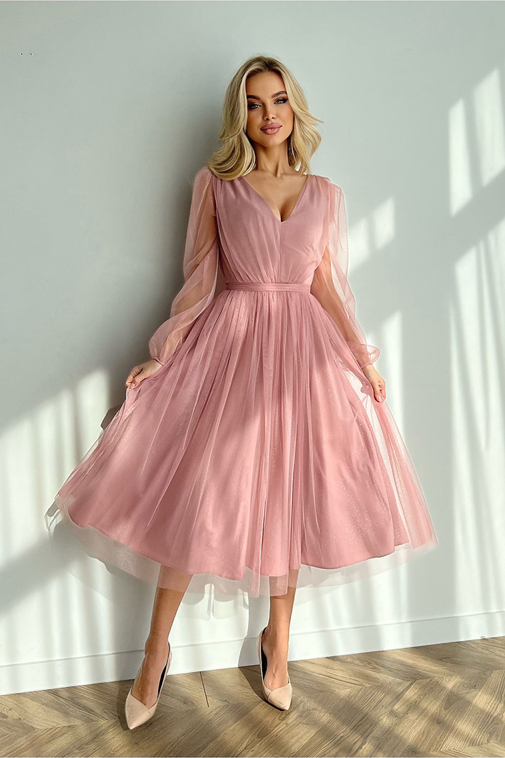 Woman wearing Marleia Mesh-Layered Evening Midi Dress in pink with sheer sleeves and flared skirt, standing against a sunlit wall.