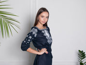 Woman wearing dark blue linen embroidered Ukrainian vyshyvanka dress with Alatyr symbol, featuring white cross-stitch patterns.