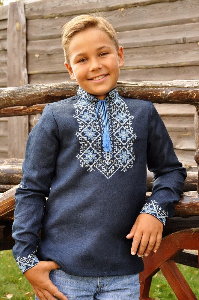 Boy wearing dark blue linen Ukrainian vyshyvanka shirt with Alatyr symbol embroidery, showcasing traditional Slavic designs.