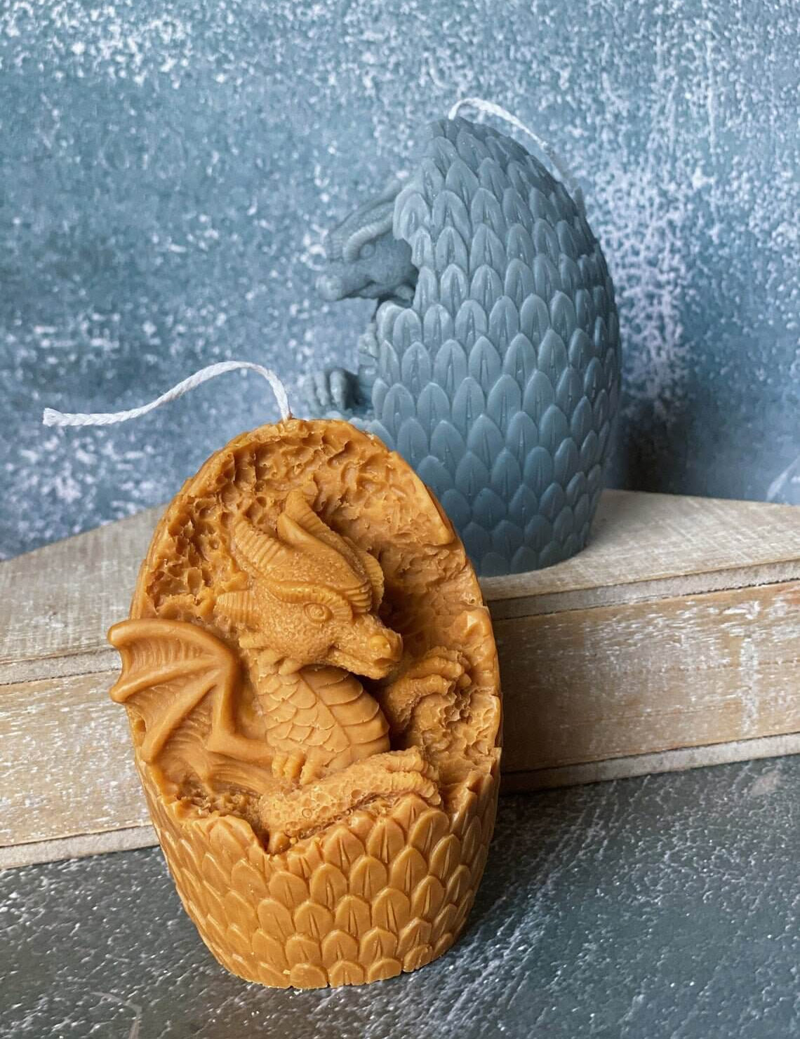 Two handmade dragon's egg candles, one carved open showing a dragon, crafted from natural soy wax with textured scales in various colors.