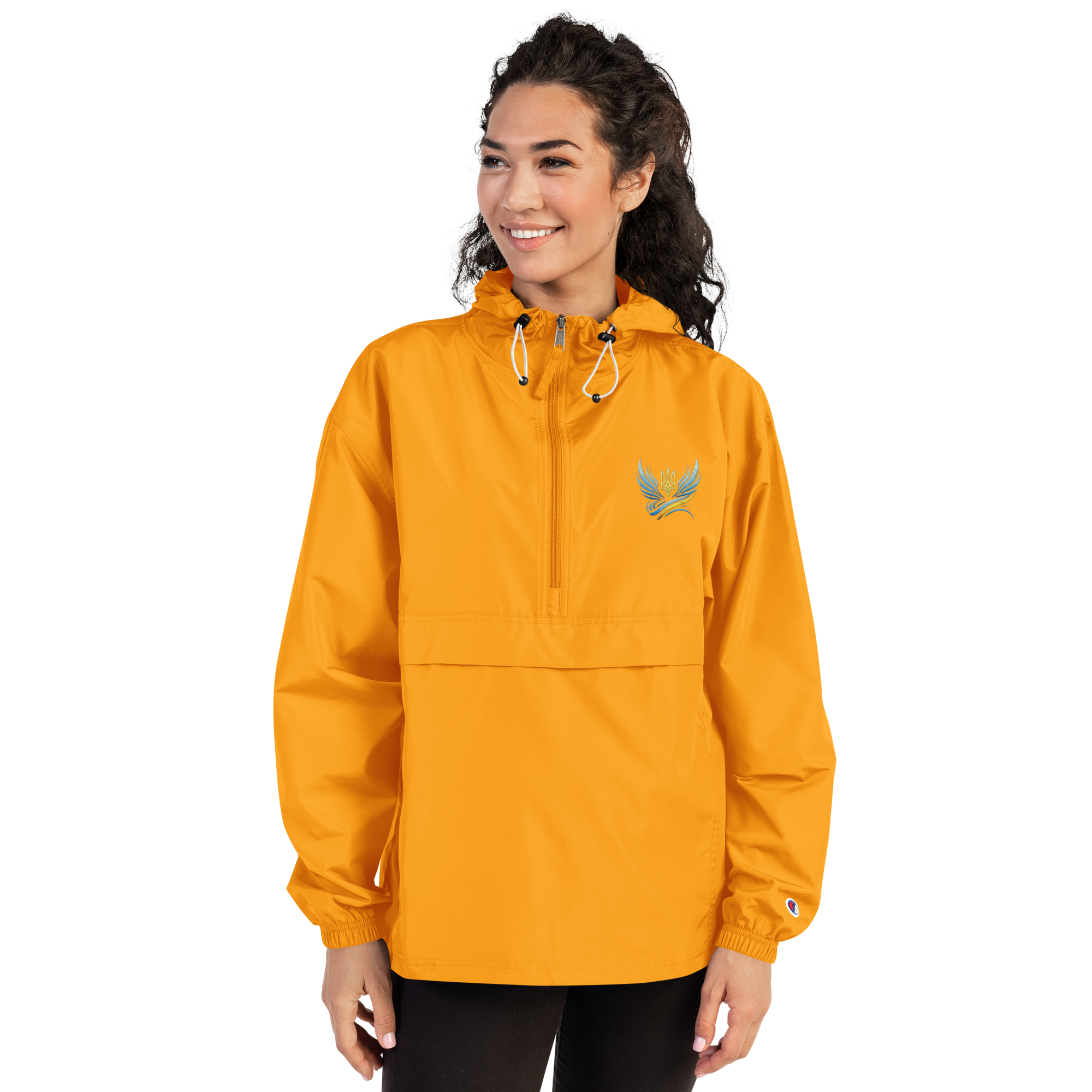 Woman wearing an orange embroidered Champion packable jacket from the Ukrainian Vibe Trizub Collection, featuring a hood and kangaroo pocket.