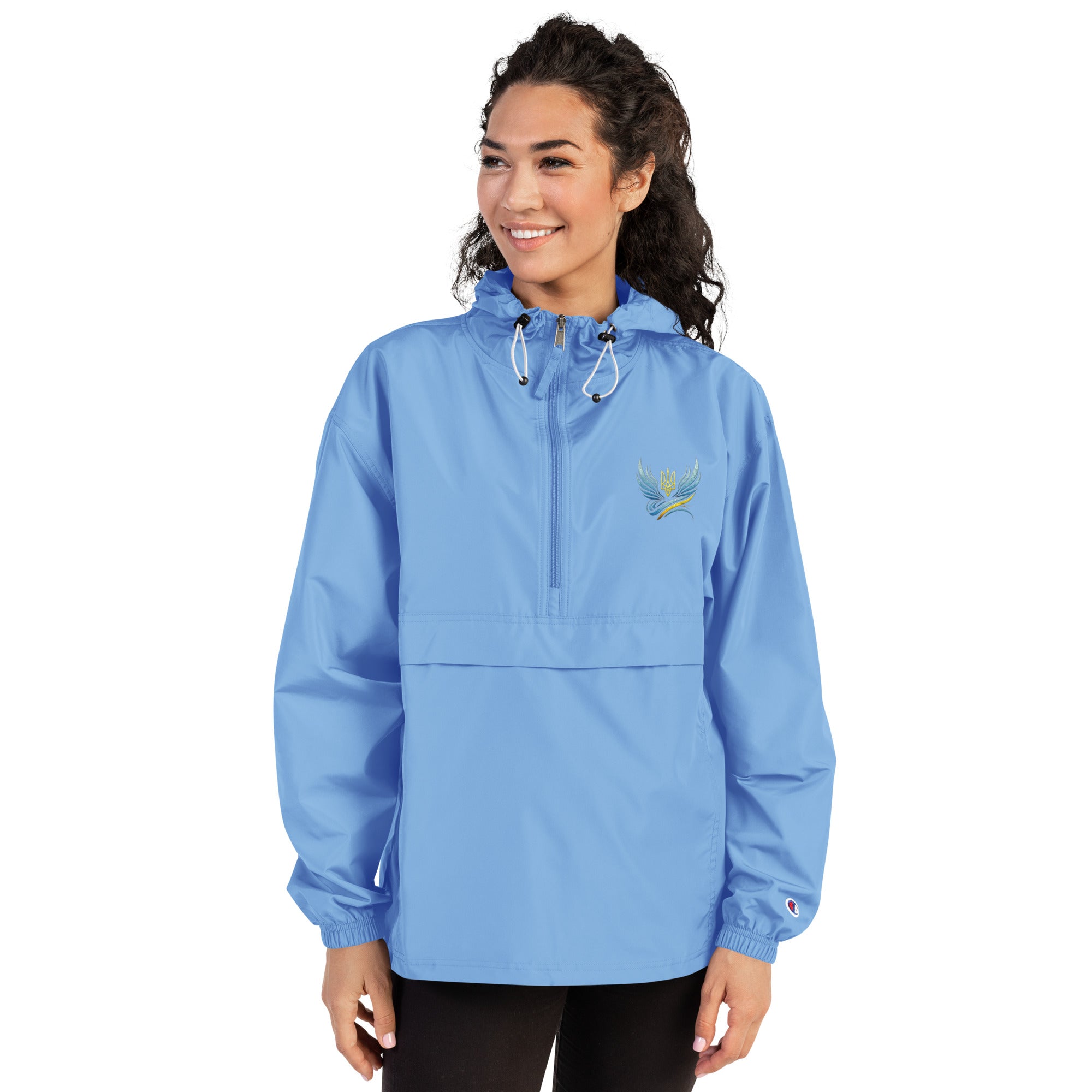 Woman wearing blue Ukrainian Vibe Trizub Collection embroidered Champion packable jacket with hood and front pockets.