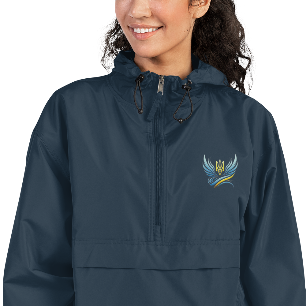 Woman wearing Ukrainian Vibe Trizub embroidered blue Champion packable jacket with hood, front pocket, and Trizub emblem.