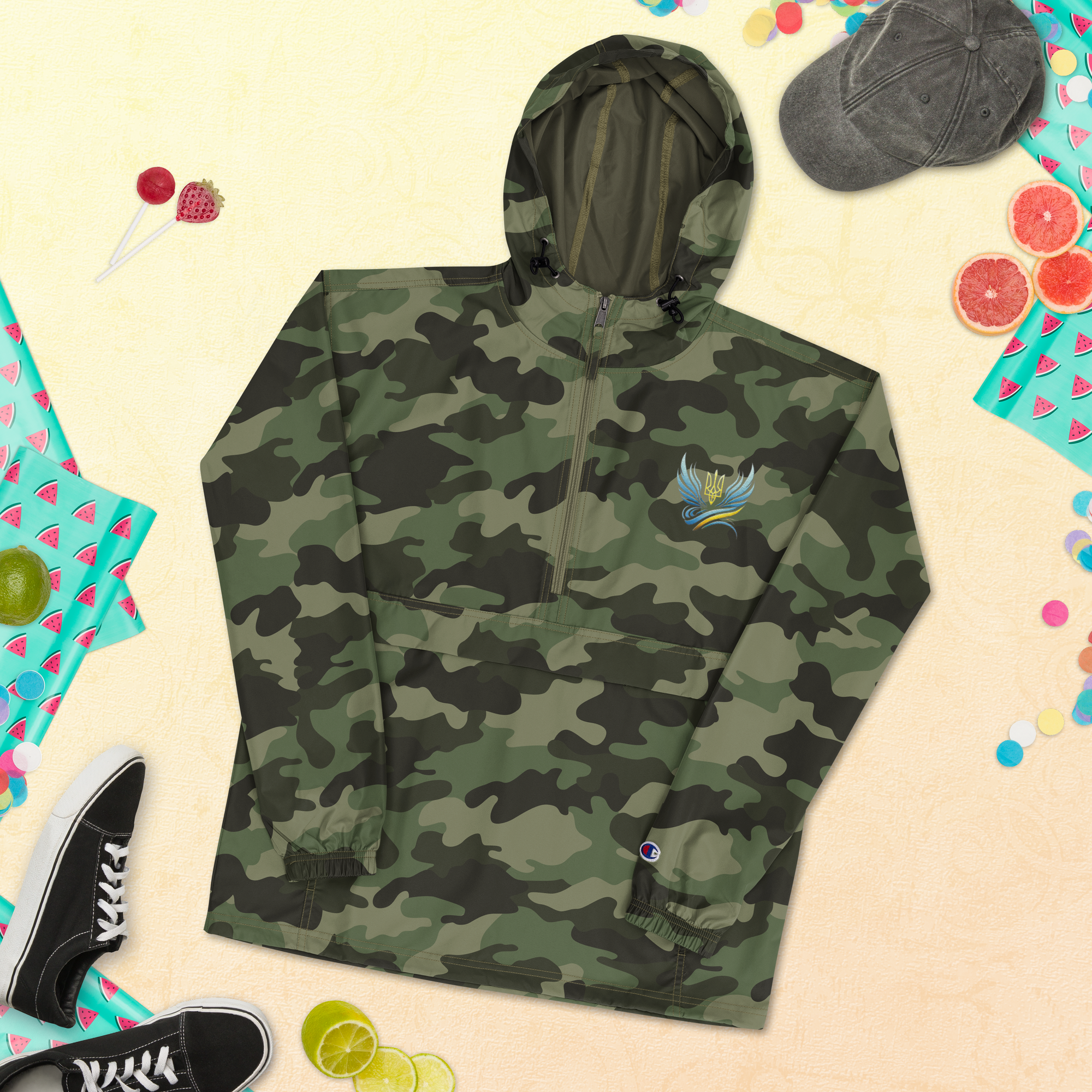 Camouflage Champion packable jacket from Ukrainian Vibe Trizub Collection with embroidered emblem, shown with shoes and summer accessories.