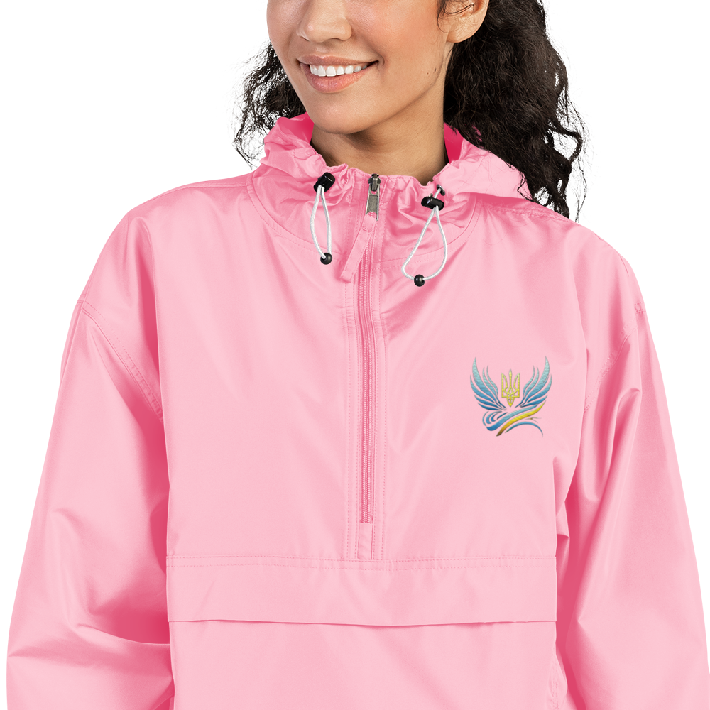 Woman wearing pink embroidered Champion packable jacket from Ukrainian Vibe Trizub Collection with hood and pouch pocket.