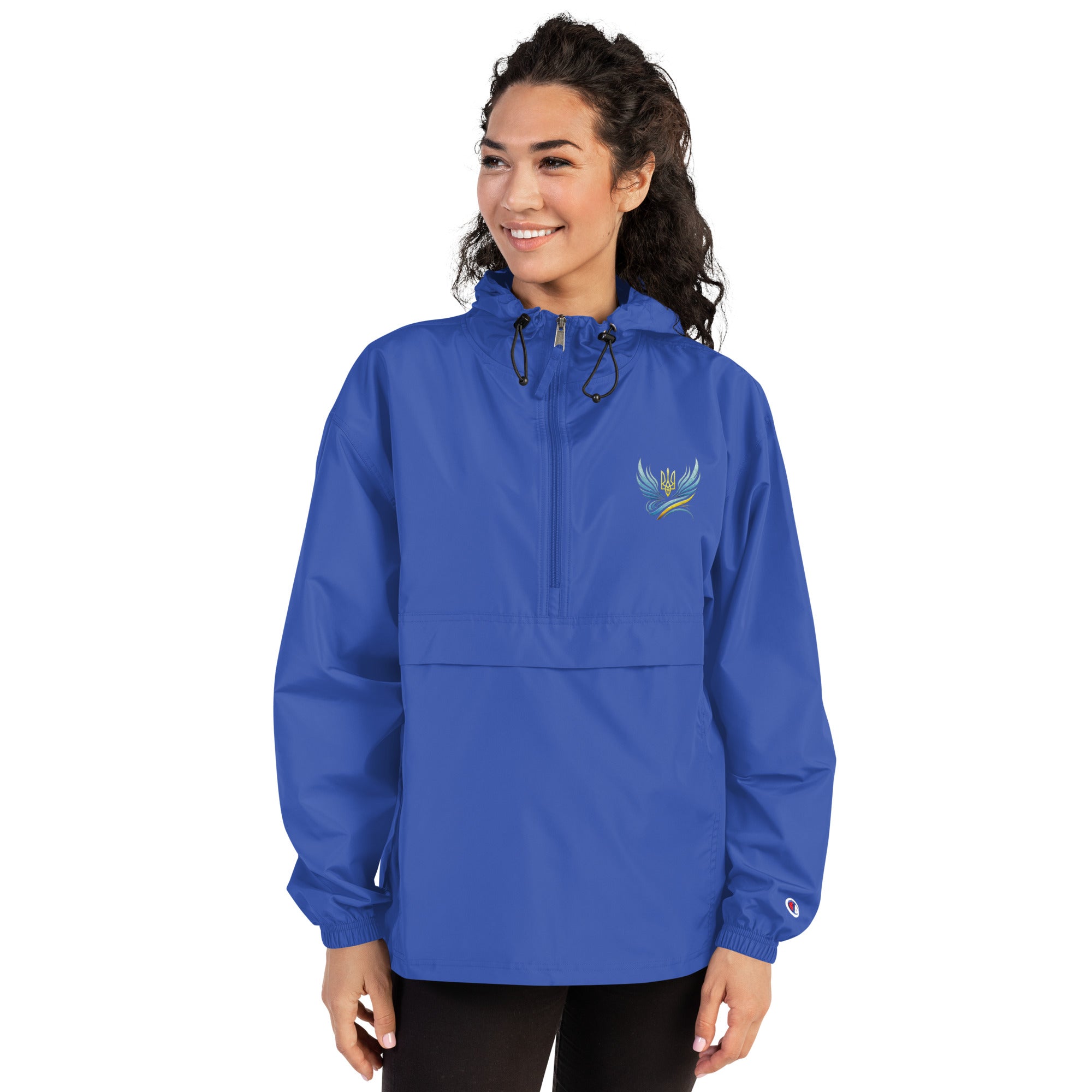 Woman wearing blue Champion packable jacket with Ukrainian embroidery from the Trizub Collection, featuring hood and kangaroo pocket.