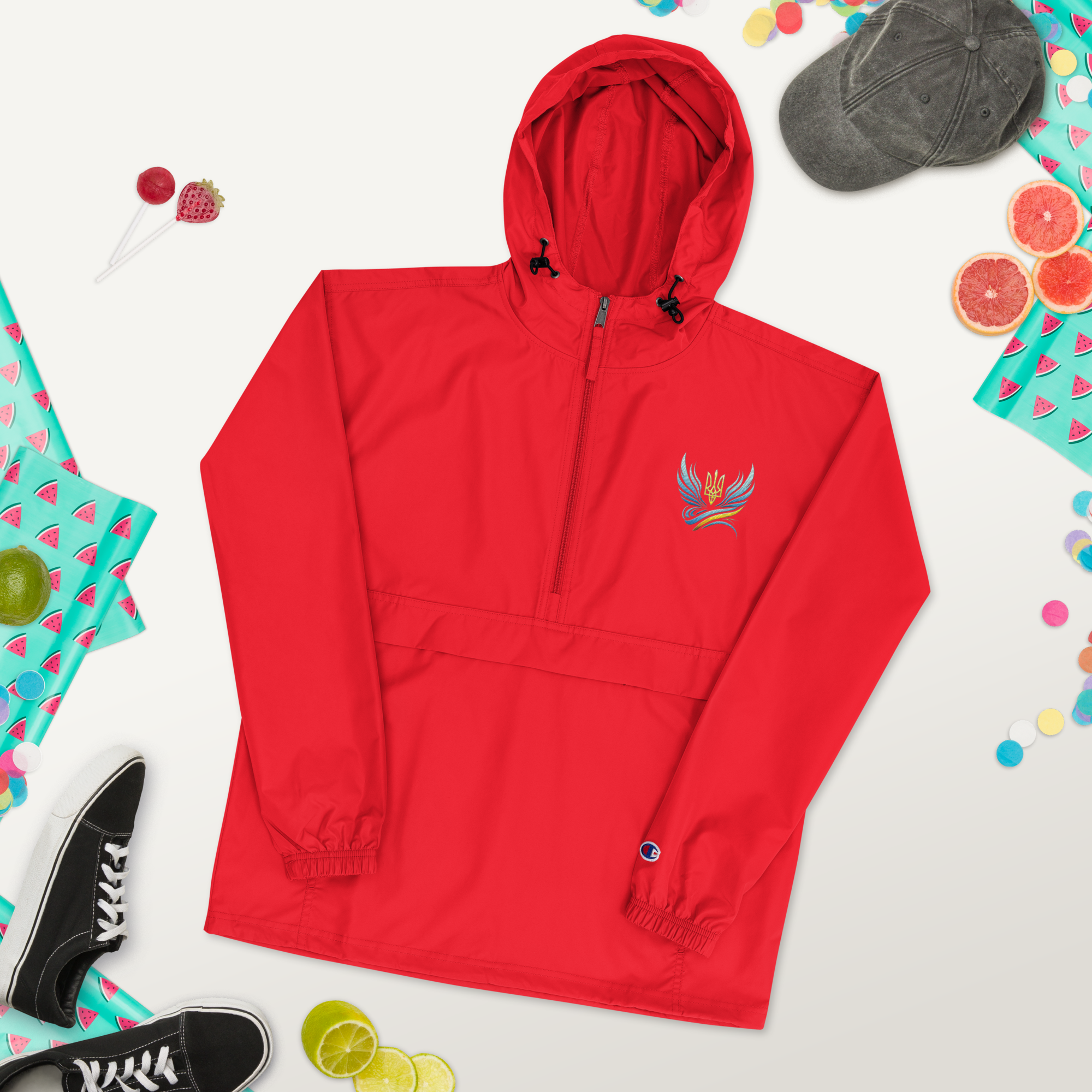 Red embroidered Champion packable jacket from Ukrainian Vibe Trizub Collection with hood and pouch pocket, surrounded by accessories.
