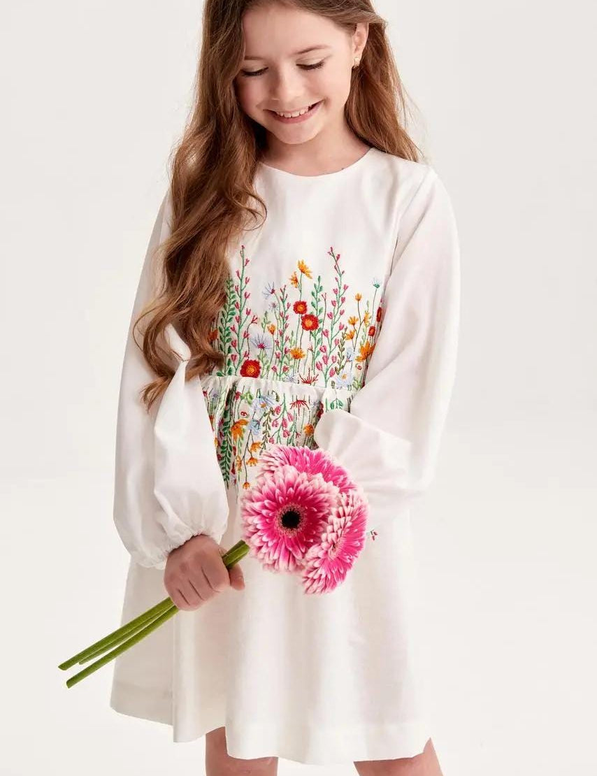 Young girl wearing embroidered linen dress with Ukrainian floral design, holding a pink flower, perfect for special occasions and birthdays.