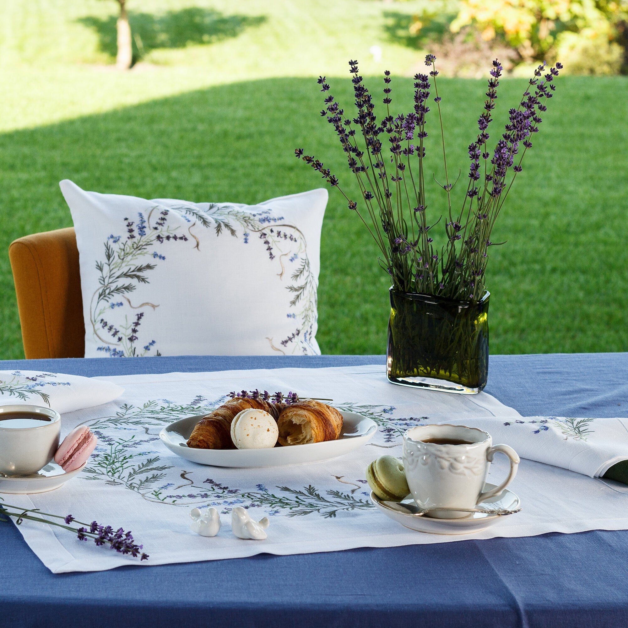 Beautifully embroidered lavender design linen tablecloth on a dining table, with tea set, pastries, and lavender bouquet.
