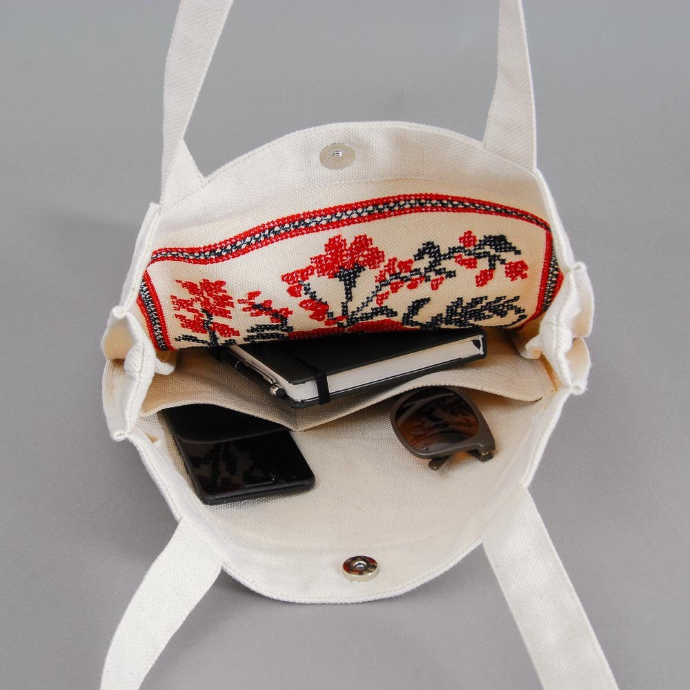 Embroidered floral linen tote bag showing interior space with phone, sunglasses, and notebook.