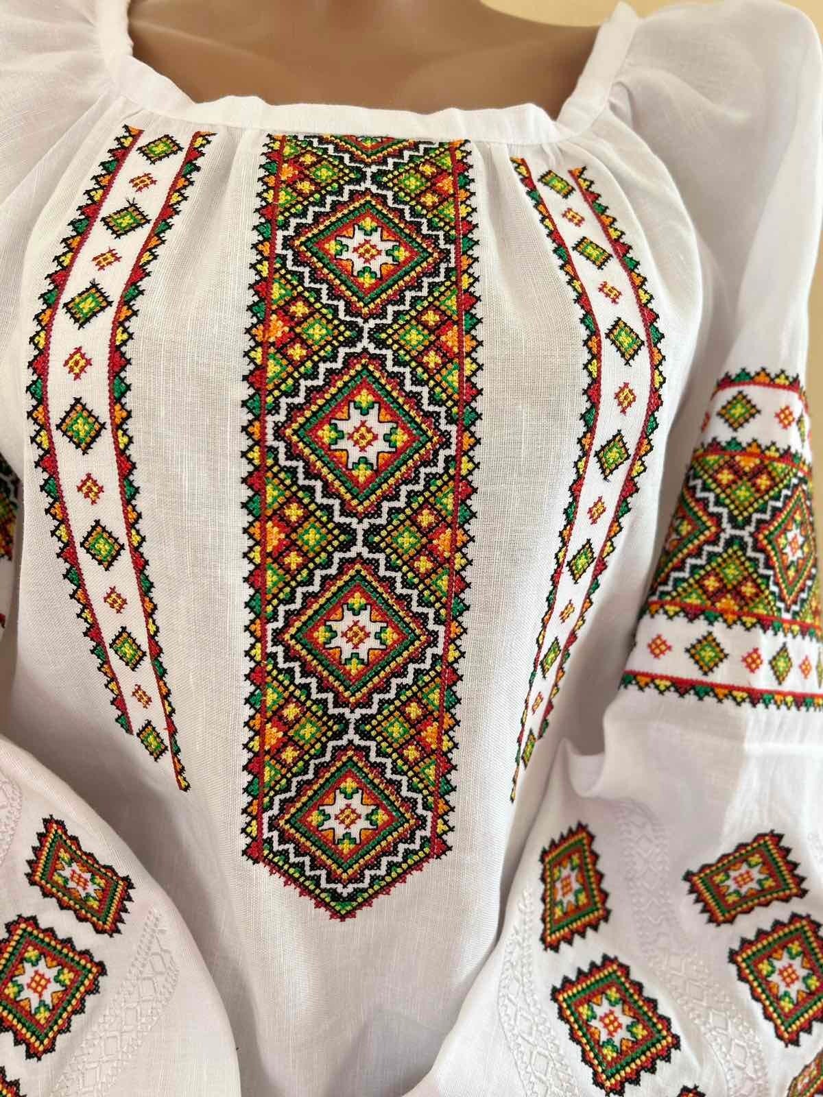 Front view of embroidered linen Vyshyvanka blouse featuring Ukrainian folk cross-stitch patterns on white fabric.