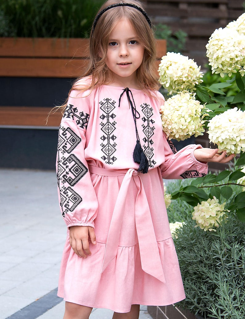 Girl wearing embroidered Vyshyvanka dress with Ukrainian patterns, pink linen-viscose, perfect for cultural occasions.