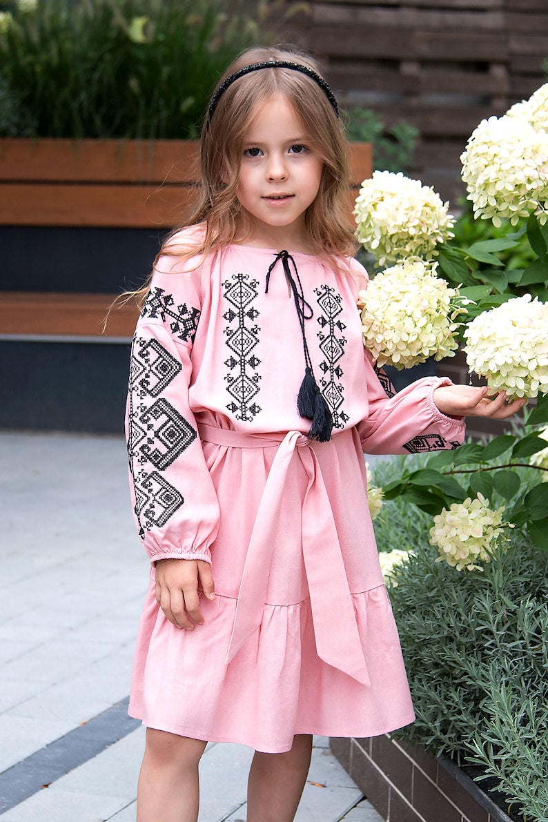 Girl wearing embroidered Vyshyvanka dress with Ukrainian patterns, pink linen-viscose, perfect for cultural occasions.