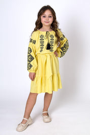 Girl wearing yellow embroidered Vyshyvanka dress with Ukrainian cross-stitch patterns and long sleeves.