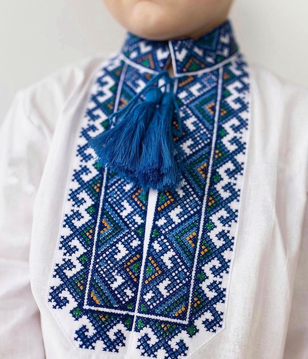 Boy wearing an embroidered Ukrainian vyshyvanka shirt with blue tassels and traditional patterns.
