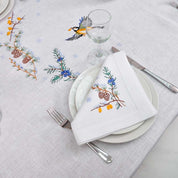 Embroidered linen tablecloth 'First Snow' with bird and pine motif, set for an elegant dinner, ideal for 8 to 12 guests.