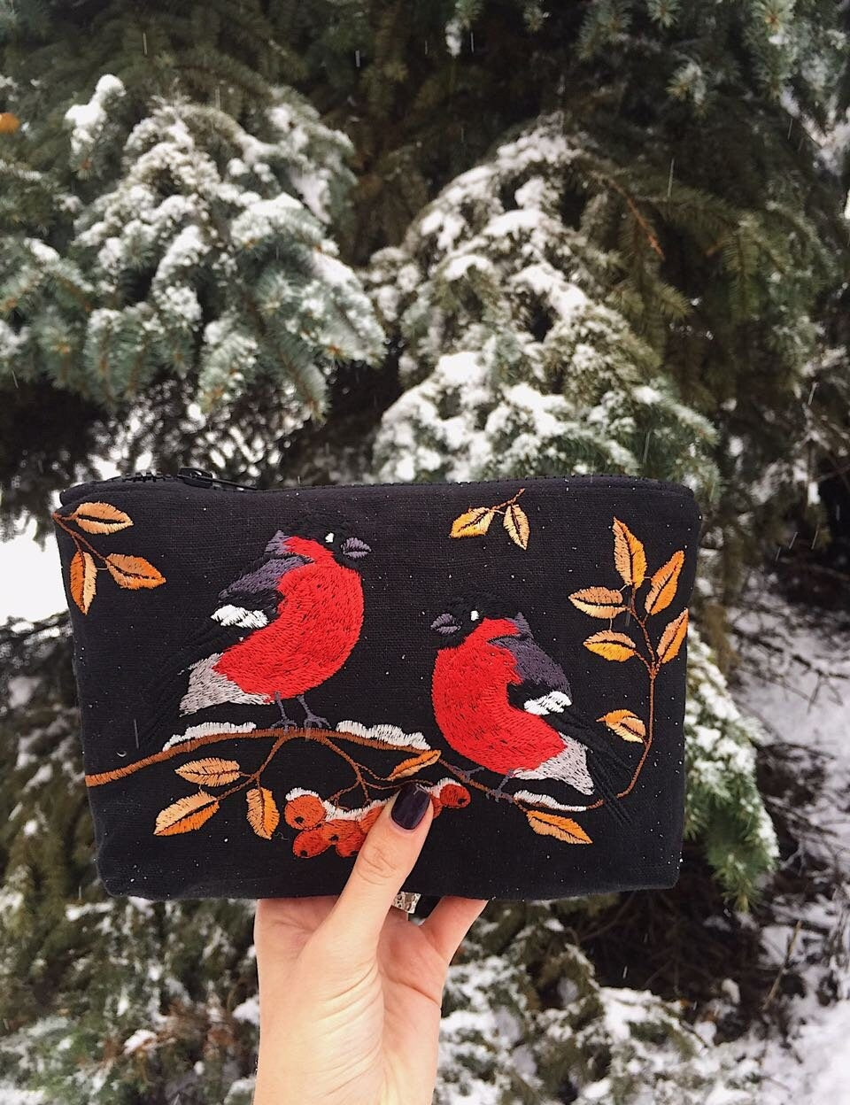 Holding an embroidered makeup bag with Ukrainian folk bird pattern in a snowy forest background, ideal gift for women.