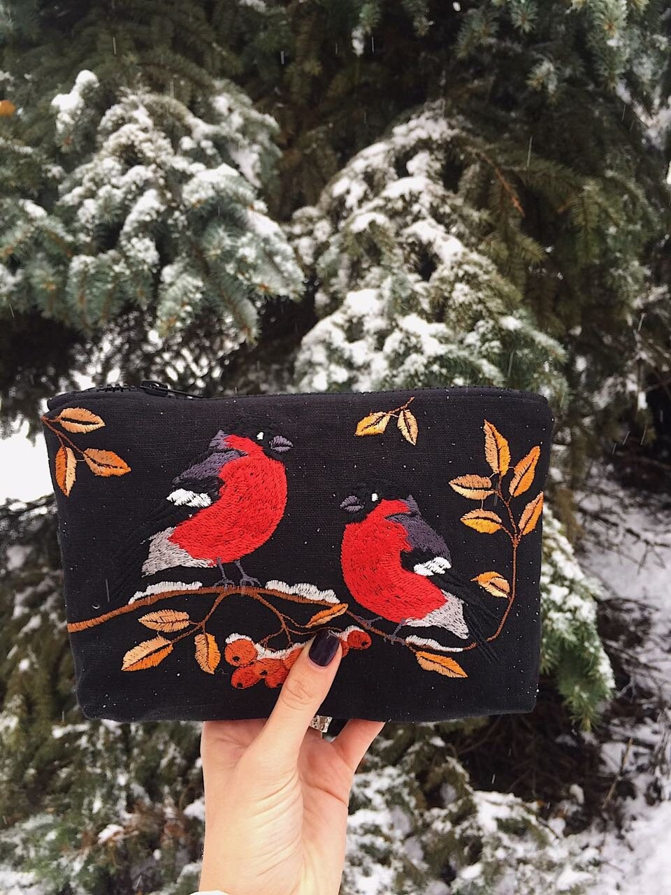 Holding an embroidered makeup bag with Ukrainian folk bird pattern in a snowy forest background, ideal gift for women.