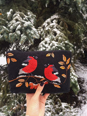 Holding an embroidered makeup bag with Ukrainian folk bird pattern in a snowy forest background, ideal gift for women.