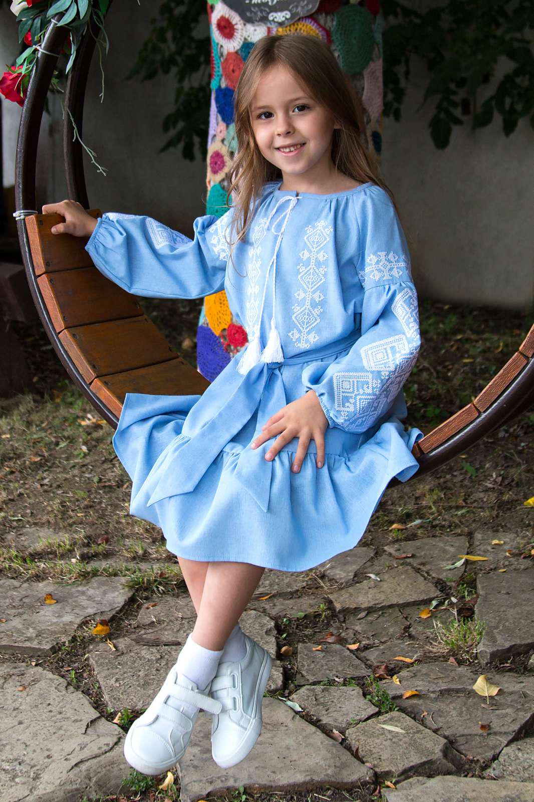 Girl in blue embroidered vyshyvanka dress with traditional Ukrainian pattern, sitting on a swing.