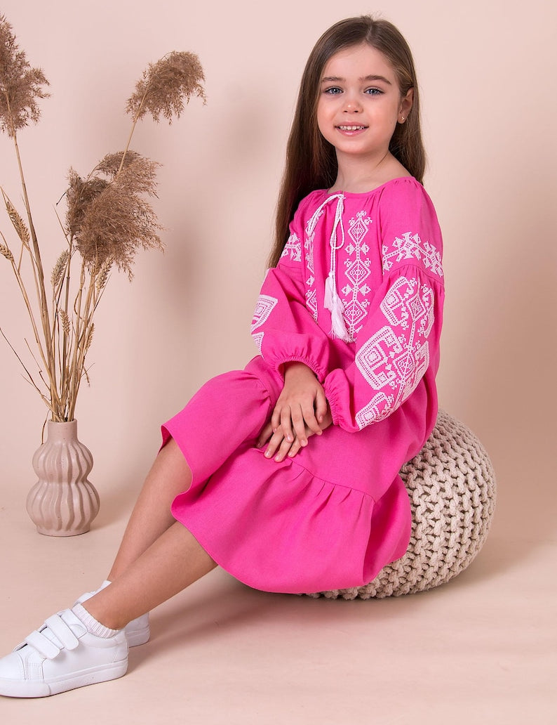 Girl wearing pink embroidered vyshyvanka dress with Ukrainian folk patterns. Linen-viscose material, perfect for cultural events.
